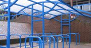 Cycle shelter for a public area. There are custom cast bicycles in the centre of the shelter and also at the top of the shelter there is a large covered roof.